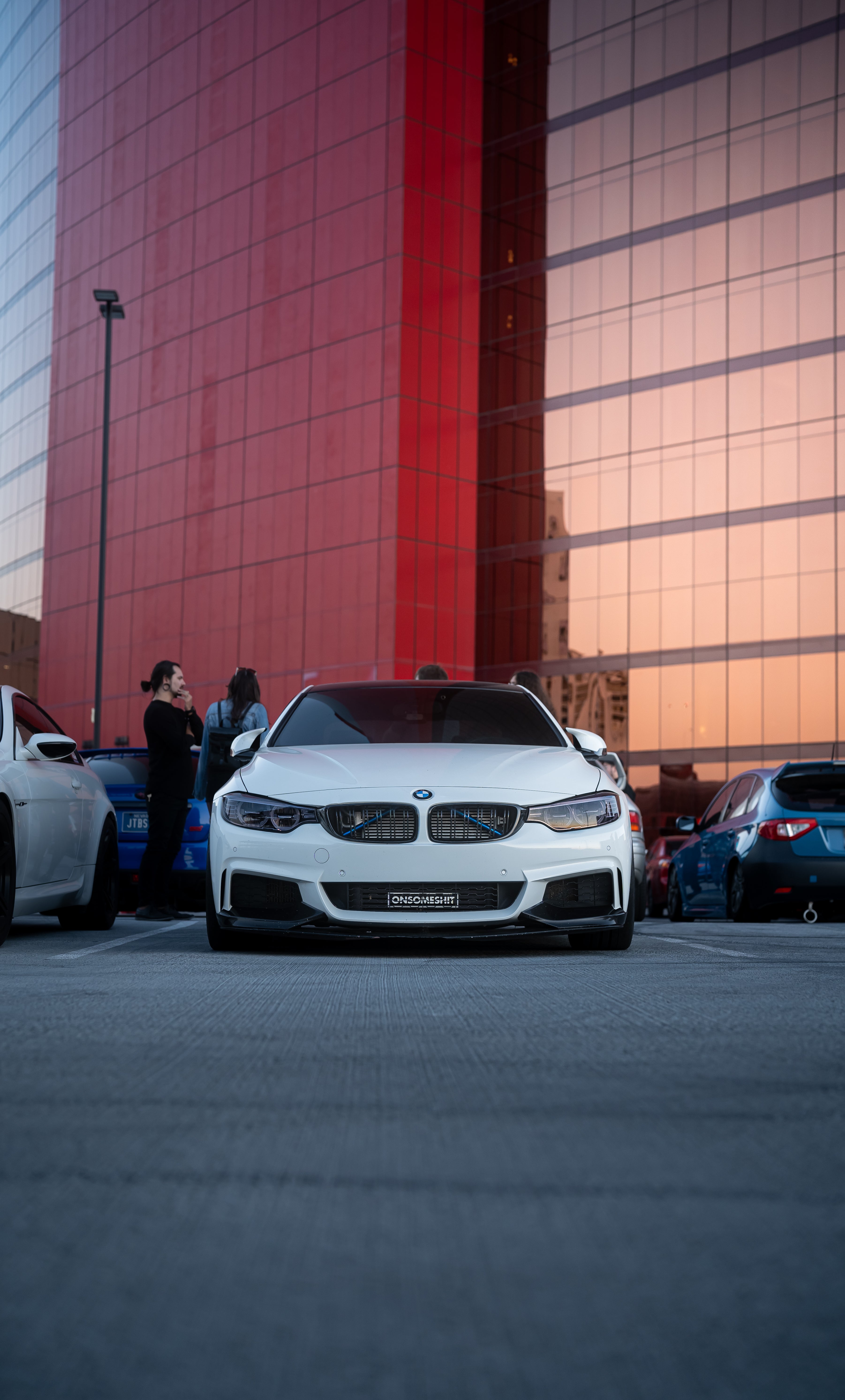 White BMW car parked in a parking lot with a red building in the background